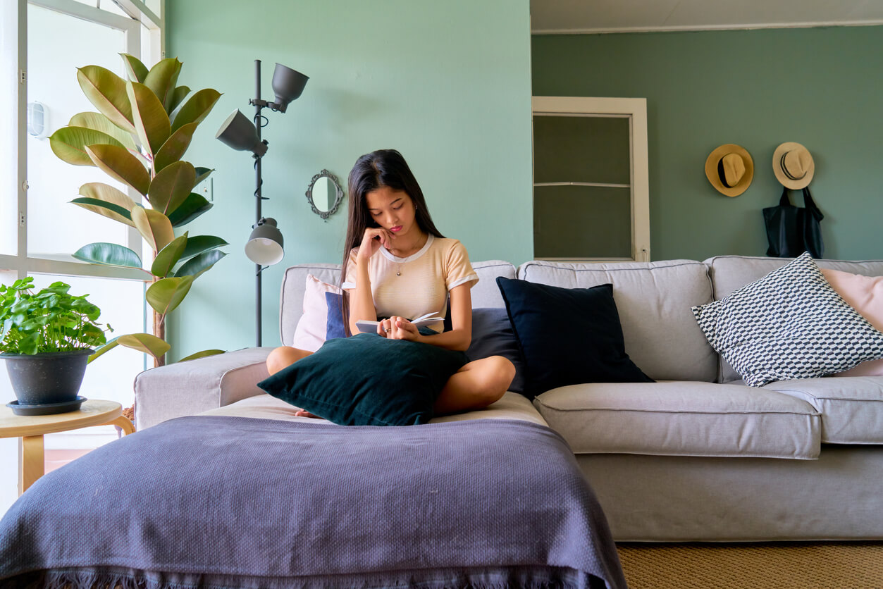 Etudiante assise dans le salon de son logement étudiant. Elle est sereine dans sa résidence étudiante à Paris 19