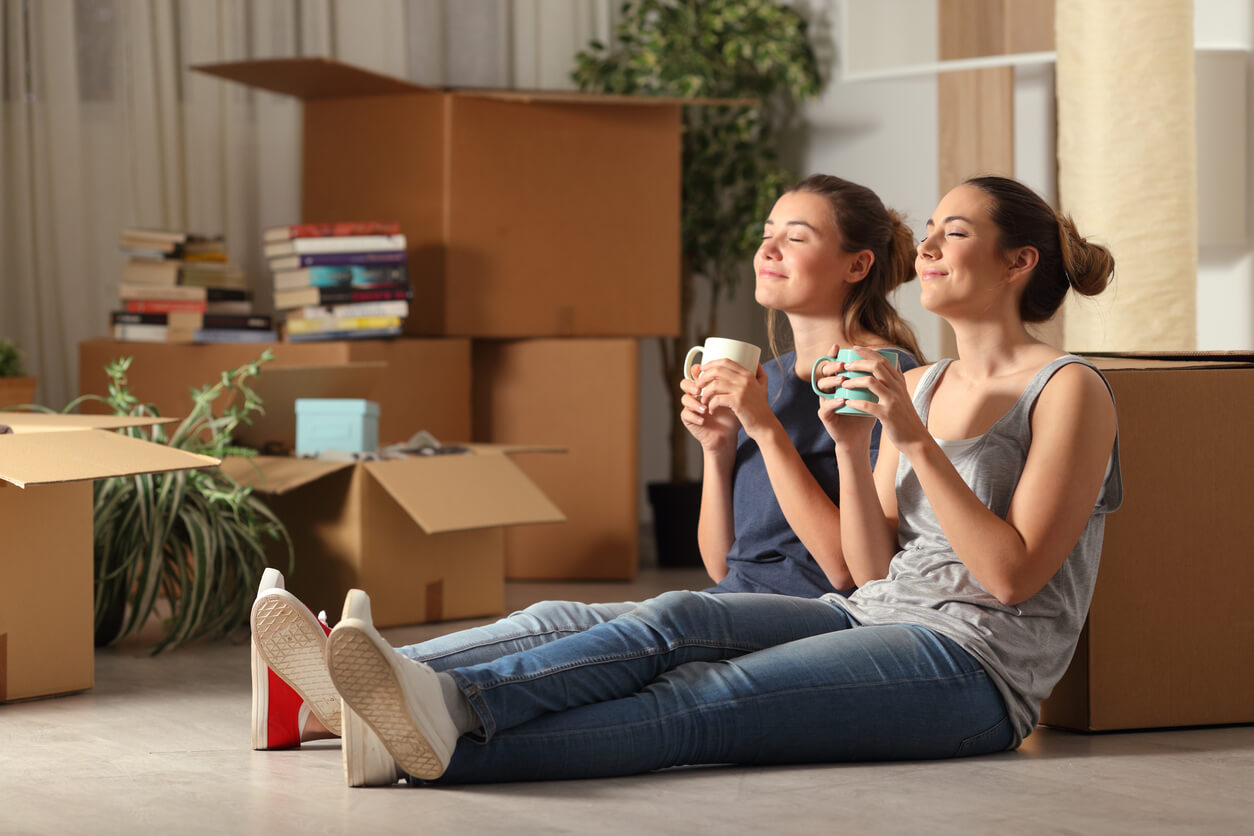 Deux jeunes étudiantes qui viennent d'emménager dans un appartement étudiant à Rennes. Elles sont assises sur le sol, une tasse à la main, appréciant la tranquillité de la ville de Rennes