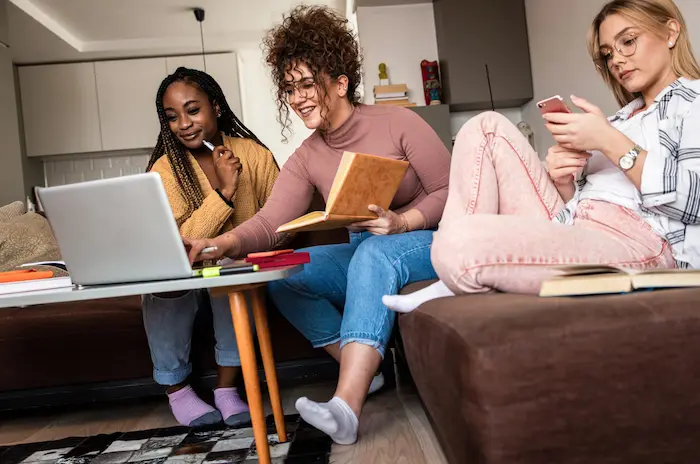 Trois étudiantes assises dans le salon d'une résidence étudiante à Paris. Elles sont en train de travailler sur le canapé dans l'espace commun de leur logement en colocation.