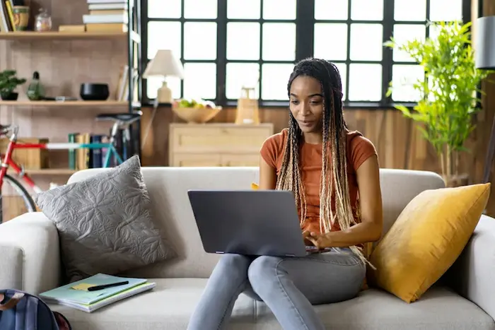 Une étudiante, heureuse devant son ordinateur, assise dans le salon de son studio en location à Paris